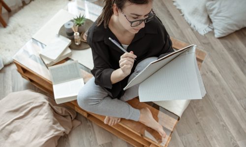 Attractive girl at home sitting with a notebook and pen among books top view.