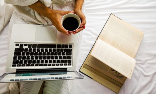 Beautiful asian woman hand holding a cup of coffee on the bed, reading a book and using computer with morning light. Relaxing concept. Retro filter effect,soft focus,selective focus.
