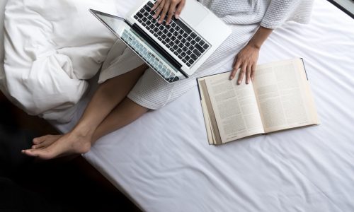 Beautiful young woman in her bed while checking her laptop at home.