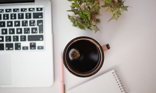 A high angle shot of cup of coffee next to silver laptop
