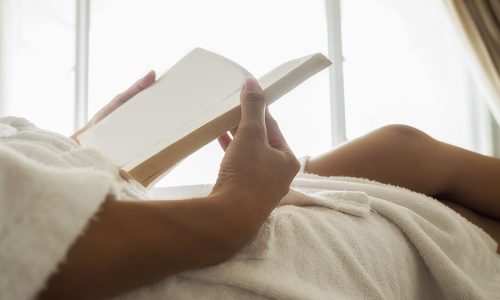 Beautiful asian female sitting on the bed with a cup of coffee and reading a book. Morning with a book and cup of coffee. Relaxing concept. Retro filter effect,soft focus,selective focus.