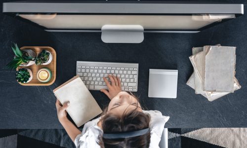 A little girl sits in front of a computer with books, top view. Studying remotely, homeschooling.