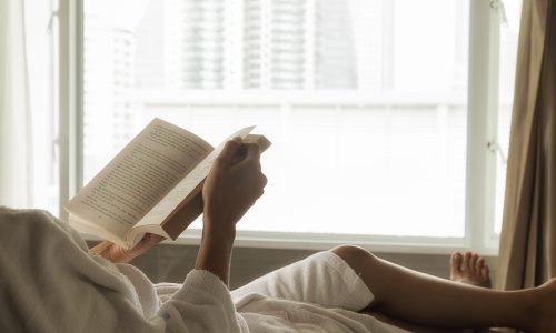 Beautiful asian female sitting on the bed with a cup of coffee and reading a book. Morning with a book and cup of coffee. Relaxing concept. Retro filter effect,soft focus,selective focus.
